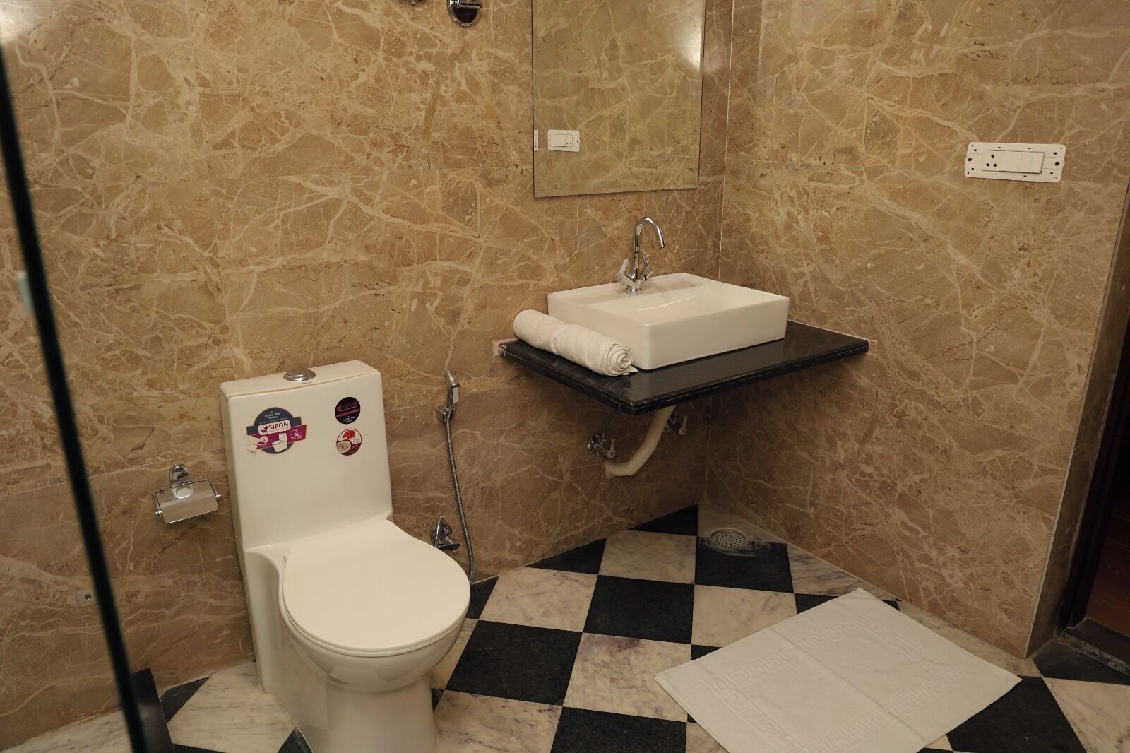 Une salle de bain avec des toilettes, un lavabo et un carrelage à motifs carrés.