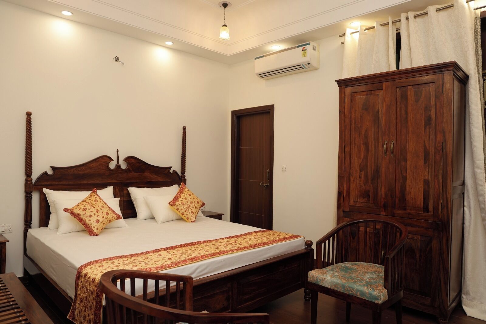 A bedroom with a four-poster bed, a wooden wardrobe, a chair, and an air conditioning unit.