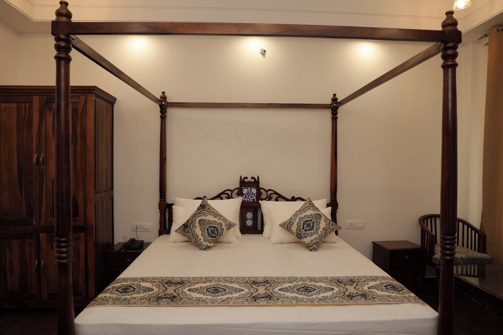 A four-poster bed with a wooden frame, a white bedspread, and patterned pillows.