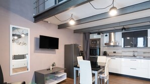 Eine moderne Küche mit weißen Schränken, einem eingebauten Backofen und einer Mikrowelle. Es gibt einen Essbereich mit einem Glastisch und weißen Stühlen.
