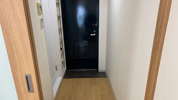 A narrow hallway with wooden flooring, a black door with a keypad lock, and a small shelf unit with a telephone and a thermostat. - W110 - Quaint Sakurashinmachi - Newly Renovated Unit with Two Beds  (Setagaya City)