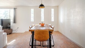 Un coin repas avec une table en bois, six chaises, une suspension et un téléviseur en arrière-plan.