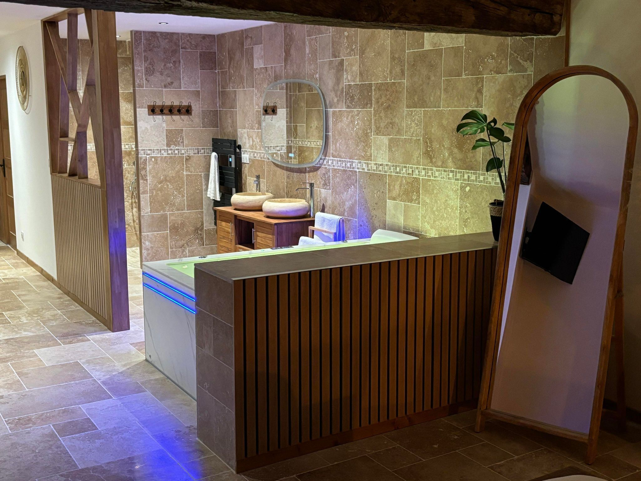 Une salle de bain moderne avec un comptoir d’accueil en bois, un grand miroir et un lavabo doté de deux cuves rondes.