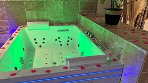 Een bubbelbad met groene verlichting, rozenblaadjes en een potplant.
