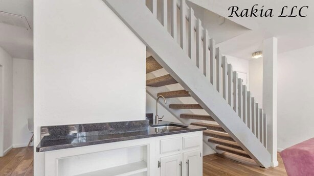 Une cuisine moderne avec des meubles blancs et un plan de travail en granit, qui donne sur un escalier en bois.