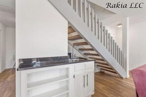 Eine moderne Küche mit weißen Schränken und einer Arbeitsplatte aus Granit, die zu einer Holztreppe führt.