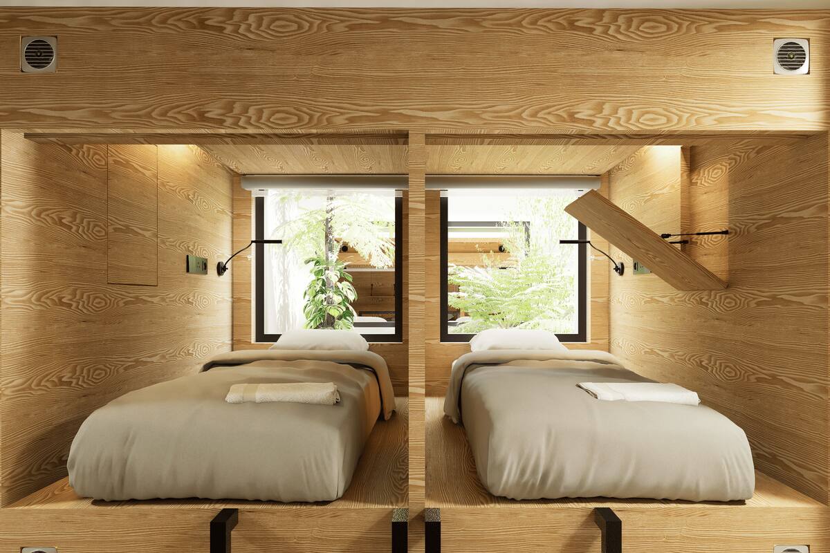A room with two beds, wooden walls, and windows with a view of greenery.