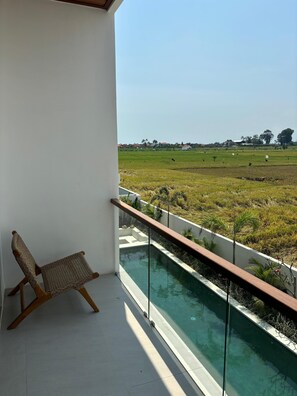 A balcony with a view of a green field and a swimming pool. - Paddy's House Seseh (Cemagi)