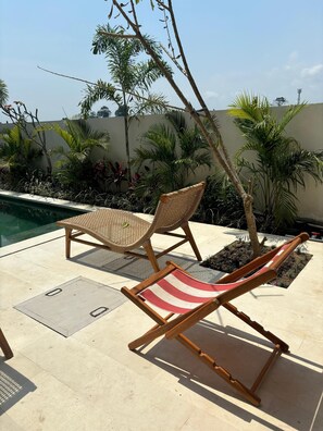 A poolside area with two wicker lounge chairs and a red and white striped beach chair. - Paddy's House Seseh (Cemagi)