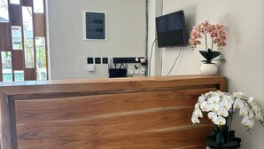 Un comptoir d’accueil avec un revêtement en bois, une caméra de surveillance fixée au mur, un téléviseur à écran plat et deux orchidées en pot.