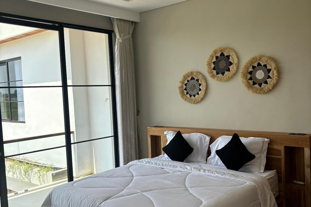 Ein modernes Schlafzimmer mit einem großen Bett, einem Holz-Kopfende und Blick auf ein Gebäude durch ein großes Fenster.