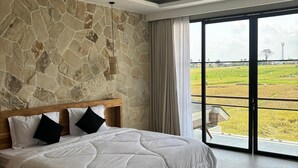 Une chambre avec un mur en pierre, un grand lit et une vue sur une rizière, accessible par une porte coulissante.