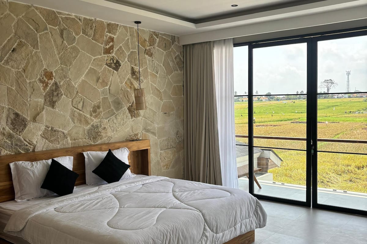 Ein Schlafzimmer mit Steinsturz, einem großen Bett und Blick auf ein Reisfeld durch eine Schiebetür.