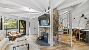 A spacious living area with a fireplace, wooden flooring, and a modern staircase. - River Cabin A-Frame-Remodeled A-Frame on the river, walk to town, lake & dining (McCall)