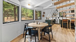 A modern kitchen with a wooden floor, white walls, and large windows overlooking a forest. - River Cabin A-Frame-Remodeled A-Frame on the river, walk to town, lake & dining (McCall)
