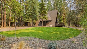 A modern house with a sloped roof, surrounded by a well-maintained lawn and a forested area. - River Cabin A-Frame-Remodeled A-Frame on the river, walk to town, lake & dining (McCall)