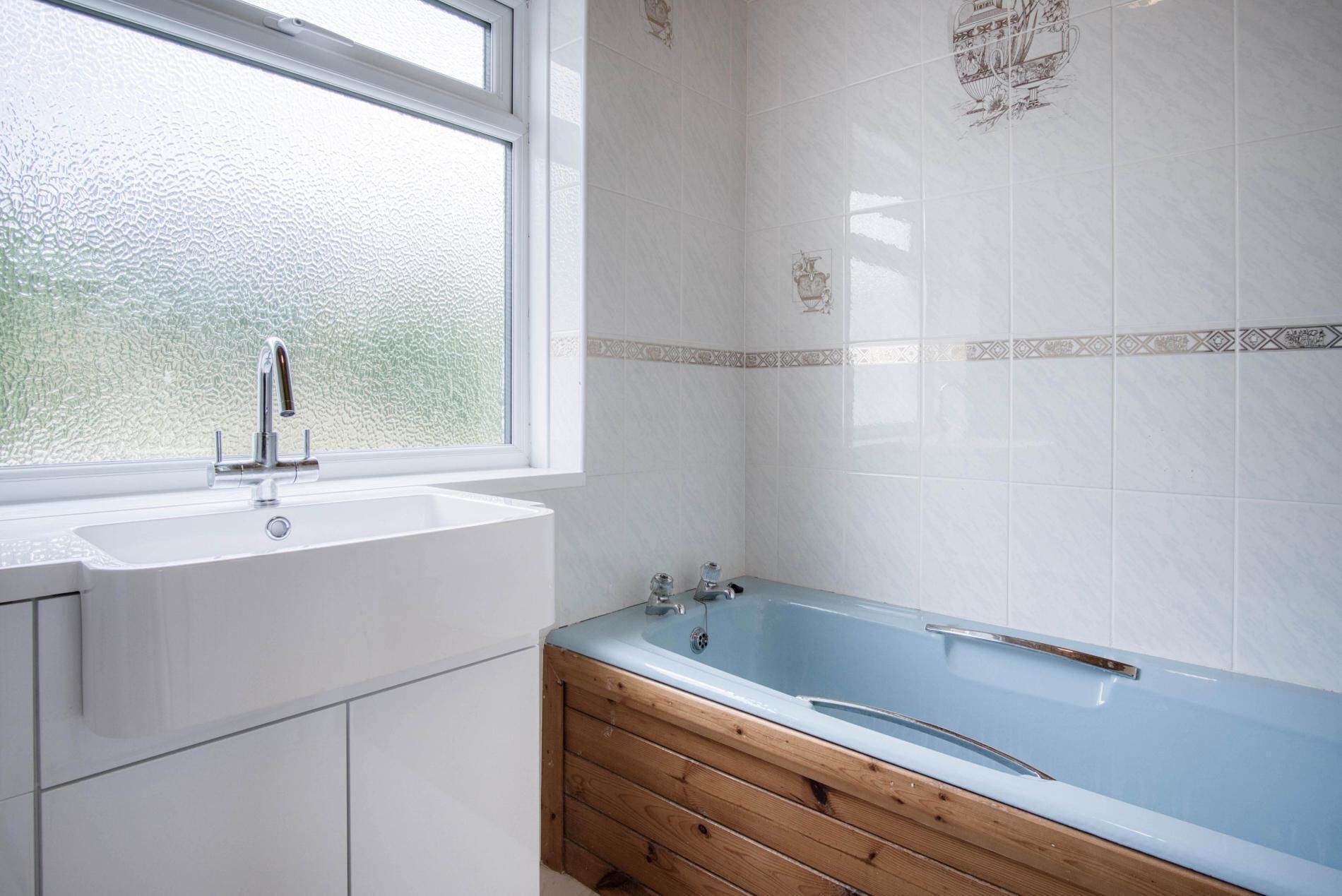 A bathroom with a white sink, a window, and a blue bathtub.