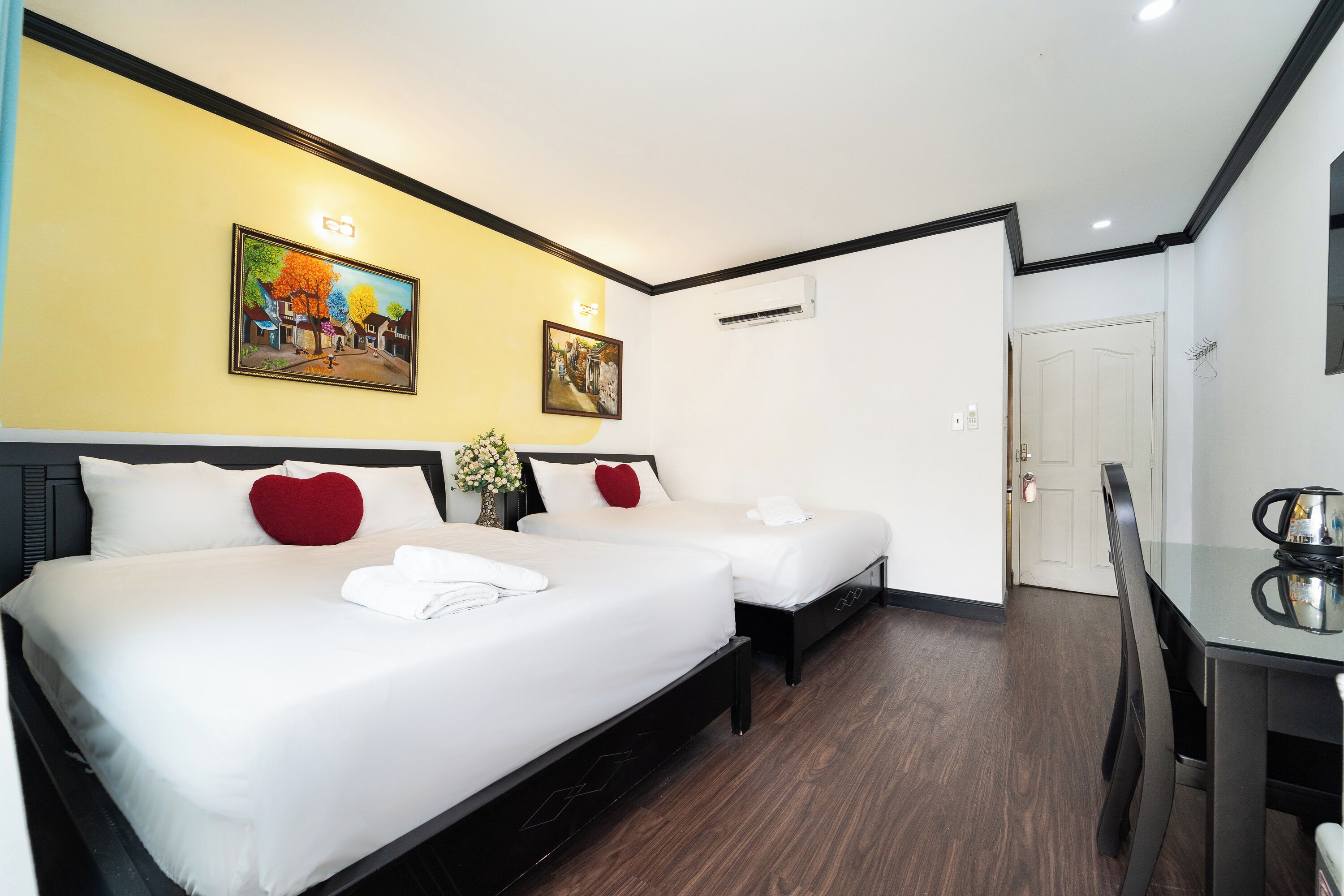 Une chambre d’hôtel avec deux lits, une table à manger et des œuvres d’art accrochées aux murs.