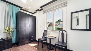 A room with a large wardrobe, a small table with chairs, a window with a view of buildings, and a mirror on the wall. - Hao Tin Hotel Ben Thanh - City Central (Ho Chi Minh City)