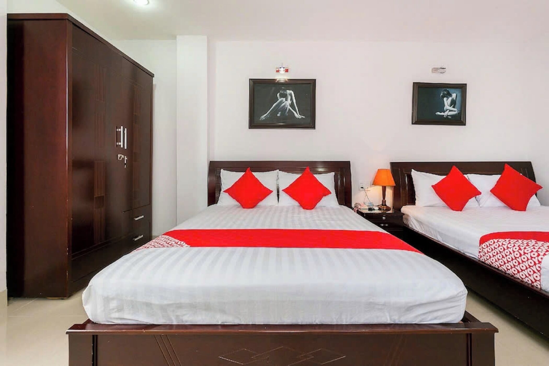 Ein Hotelzimmer mit zwei Betten, roter und weißer Bettwäsche, einem Kleiderschrank und zwei gerahmten Bildern an der Wand.
