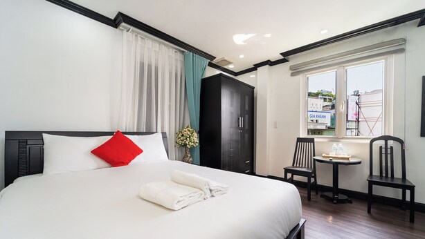 A hotel room with a large bed, a small table with two chairs, a window with a view of the outside, and a black wardrobe. - Hao Tin Hotel Ben Thanh - City Central (Ho Chi Minh City)