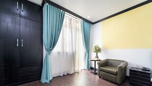 A room with dark wooden flooring, a green sofa, a small round table with a vase, and a black cabinet with drawers. - Hao Tin Hotel Ben Thanh - City Central (Ho Chi Minh City)