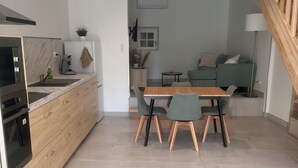 A modern kitchen with a built-in oven, a dining area with a wooden table and chairs, and a living area with a sofa and a lamp.