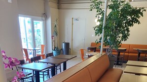 Un restaurant avec des banquettes rembourrées de tissu orange, des tables en bois et des plantes en pot.