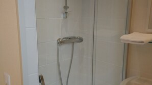 Une douche fermée par des parois en verre, dotée d’un pommeau de douche à main et d’un robinet mural.