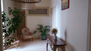 Un couloir avec une lampe en osier, une chaise, une table sur laquelle se trouve un vase, et un tableau accroché au mur.