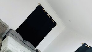 A room with a bed, a dark curtain, a white wall, and a tiled floor. - Ox Apartment (Suva)