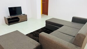 A modern living room with a sectional sofa, a flat-screen TV on a wooden stand, and a dark rug. - Ox Apartment (Suva)