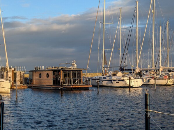 Un port de plaisance où sont amarrés plusieurs voiliers, un bâtiment en bois doté d’une petite terrasse et un ciel dégagé.