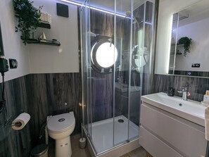 Une salle de bain moderne avec une douche à parois de verre, des toilettes blanches et un lavabo surmonté d’un miroir.
