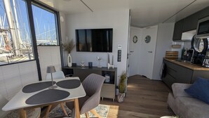 A modern living space with a dining area, kitchen, and a large window overlooking a marina. - Houseboat Fjord Stella with bio sauna and roof terrace in Wendtorf/ Kiel Fjord (Wendtorf)