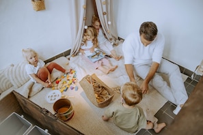 Ein Zimmer mit Spielbereich, einem Korbwägelchen und einem Eimer.