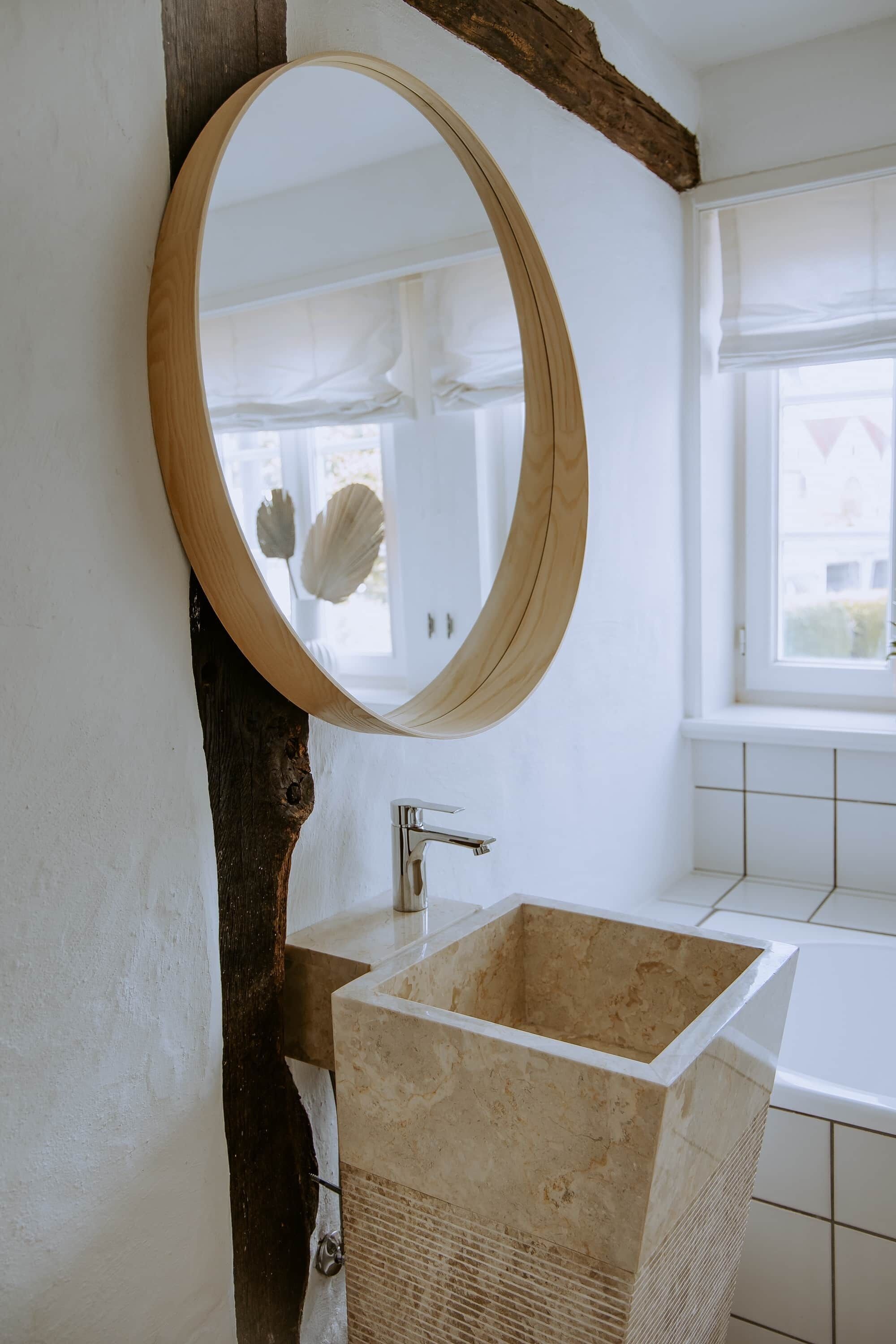 A bathroom with a wooden-framed mirror, a rectangular sink, and a window with white curtains.
