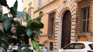 A street view with a white car parked in front of a building with a large arched doorway and barred windows. - Raffaello  (Perugia)