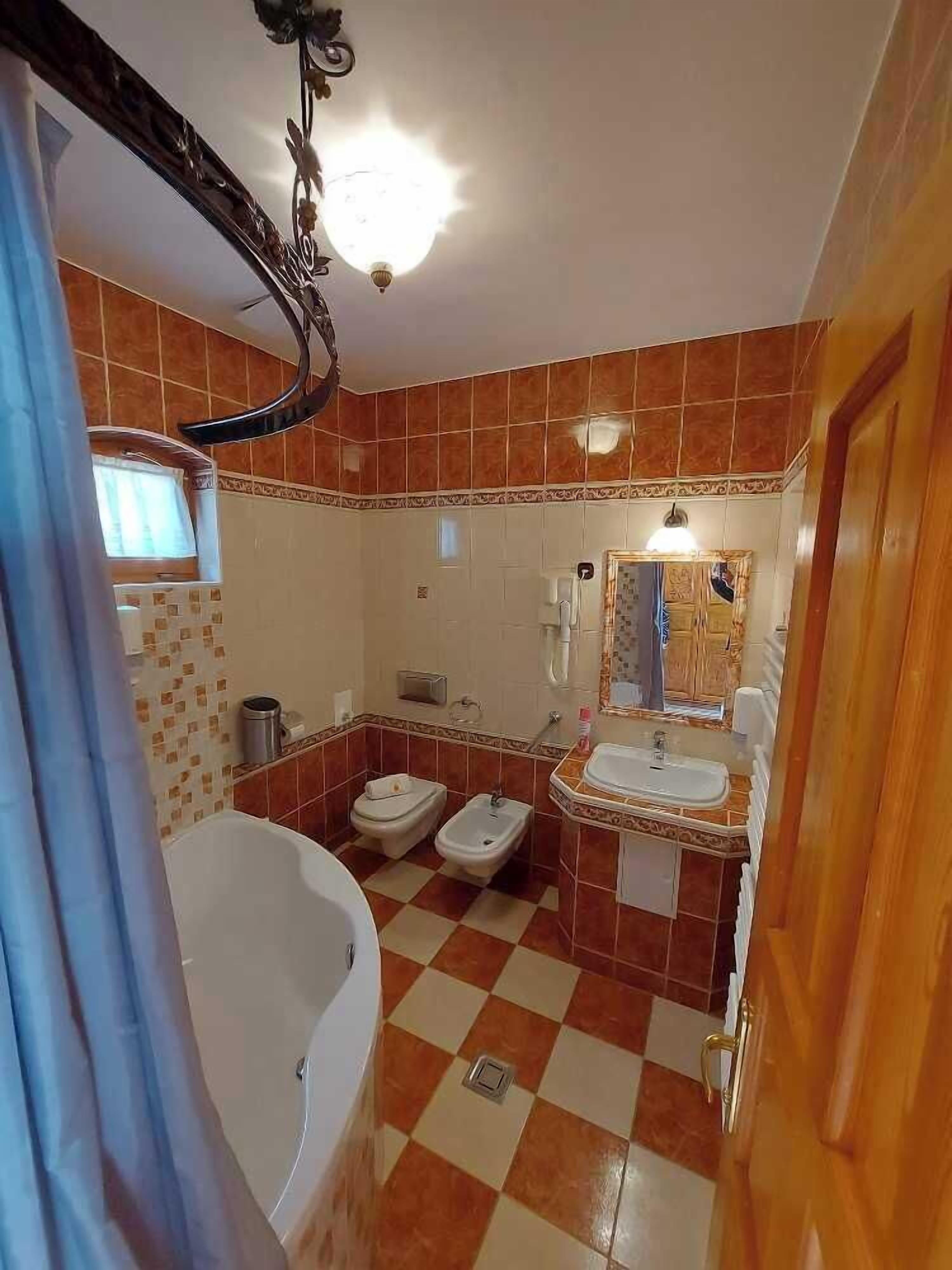 A bathroom with a checkered floor, a bathtub, two bidets, a sink, and a mirror with a decorative frame.