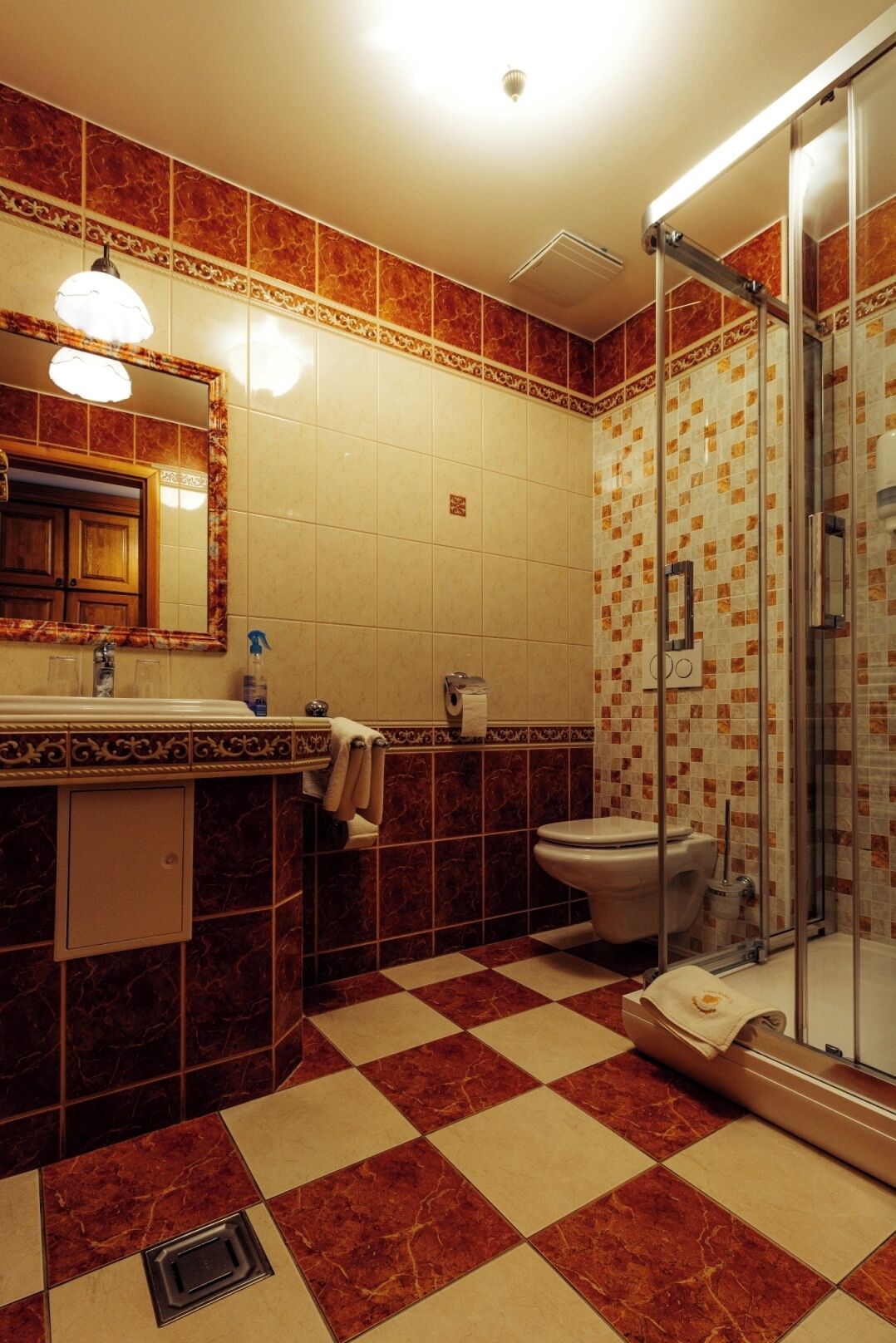 A bathroom with a checkered floor, a sink with a mirror, a toilet, and a shower with a glass door.