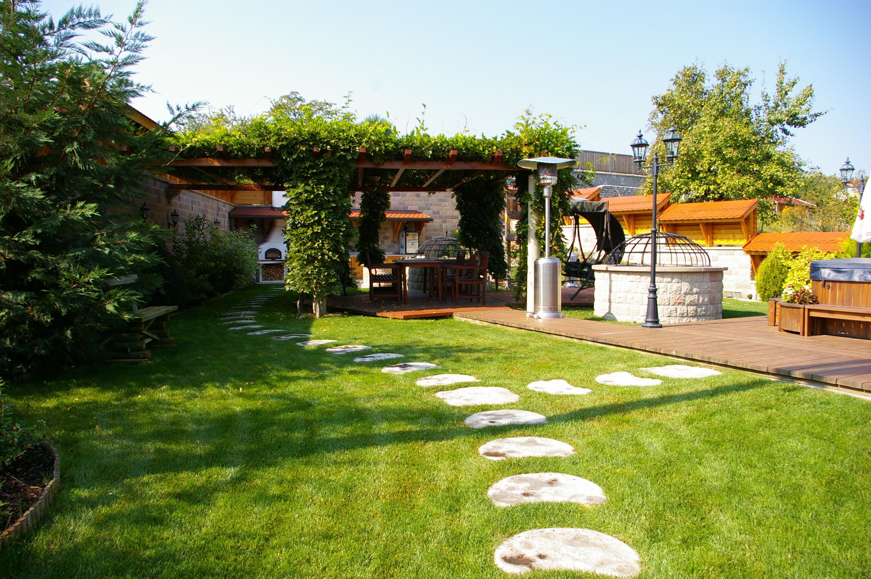 A well-maintained garden with stone stepping stones, a pergola with climbing plants, and a barbecue area.