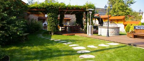 A well-maintained garden with stone stepping stones, a pergola with climbing plants, and a barbecue area.