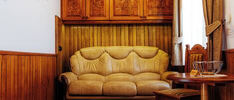 A cozy living room with a wooden ceiling, a leather sofa, a dining table with chairs, and a collection of decorative plates on the wall.