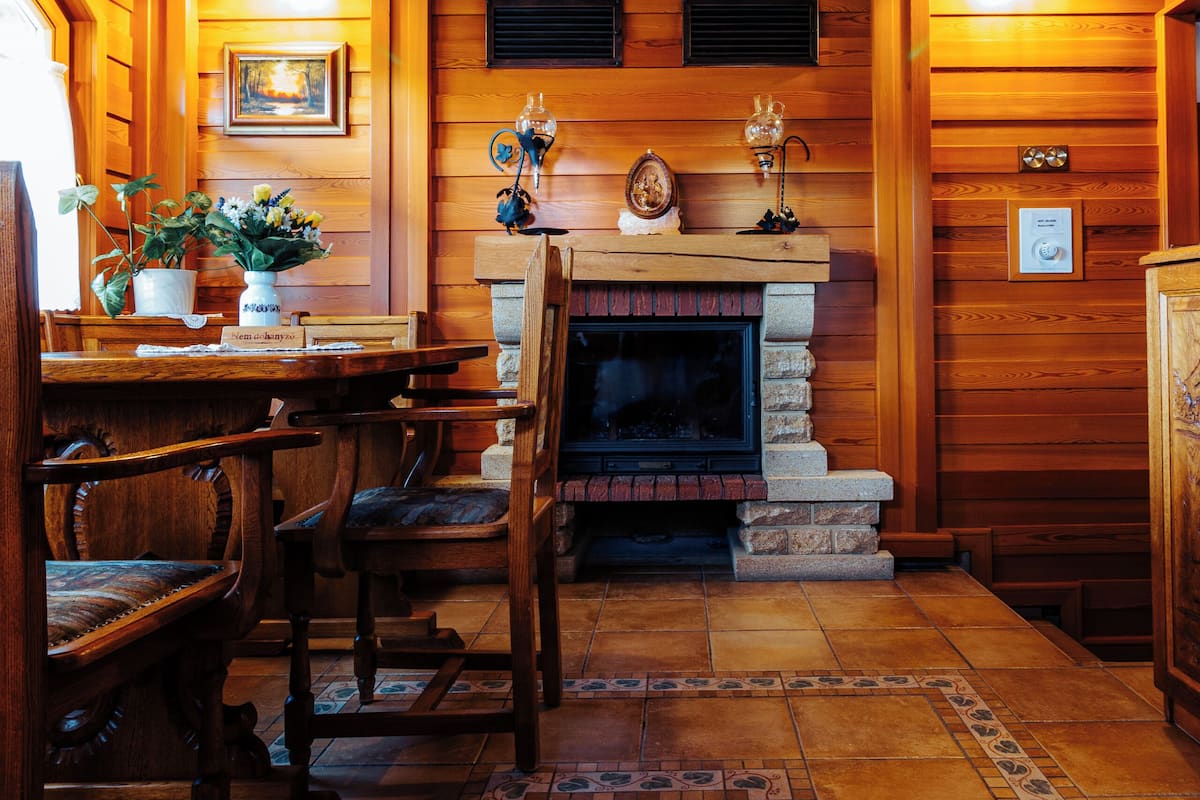 Un interior de madera con chimenea, una mesa de comedor, sillas y suelo de baldosas.