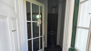 Un pasillo estrecho con una puerta blanca que da a una habitación, un muro verde y un perchero metálico al fondo.