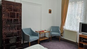 Una habitación con televisor, dos sillones, una mesita, un radiador y un aparador decorativo.