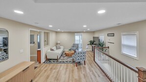Un vaste espace de vie comprenant un canapé blanc, des fauteuils à motifs, une table basse en bois et un escalier avec une rampe blanche.