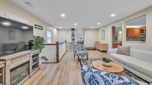 Un salon spacieux doté d’un grand téléviseur, d’un parquet, d’un canapé à motifs et d’un coin repas avec une table en bois.