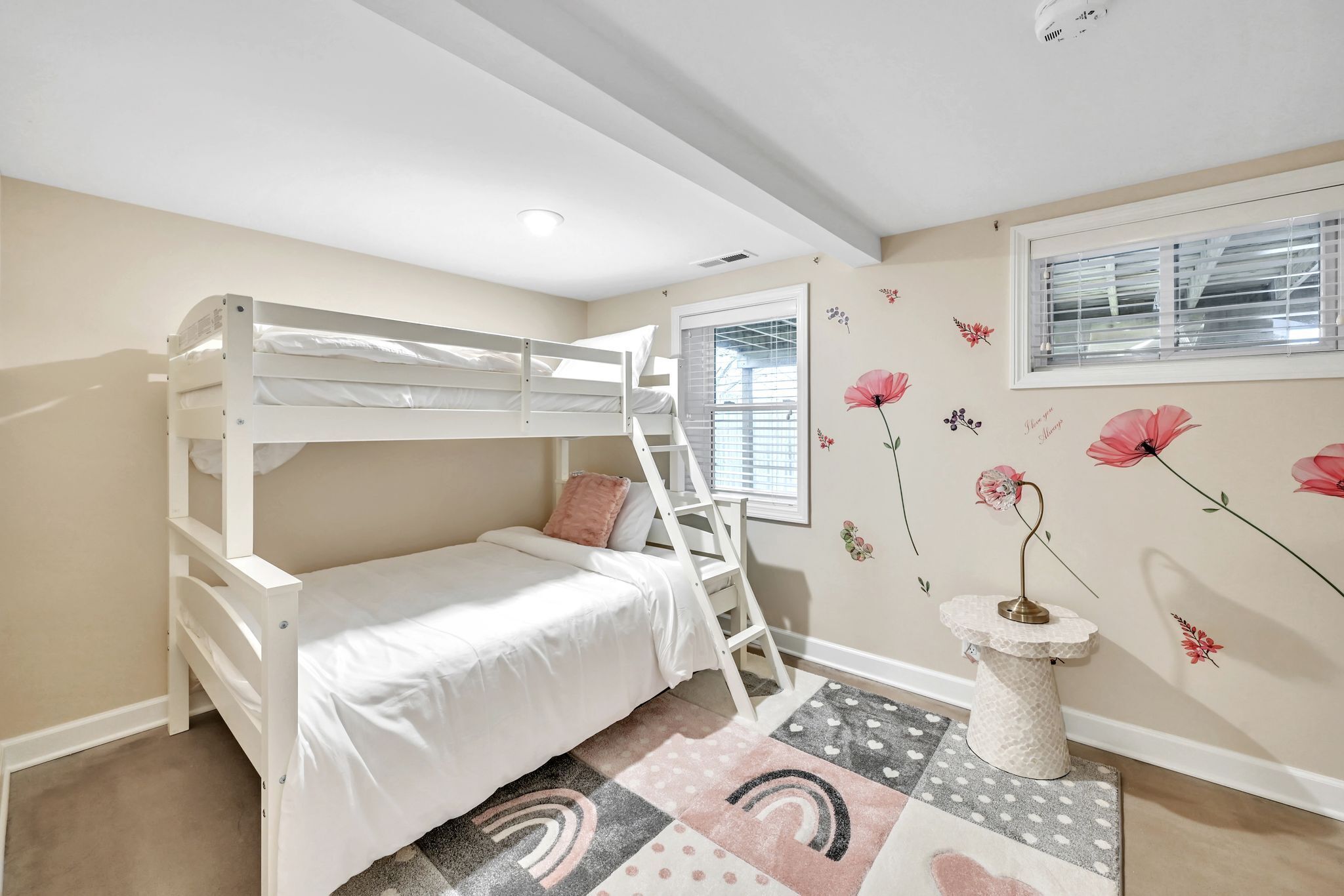 A bunk bed room with a ladder, a small table, and a window with blinds.