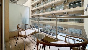 A balcony with wicker chairs, a glass table, and a view of a multi-story building with air conditioning units. - Studio With Pool and Balcony In San Telmo (Buenos Aires)